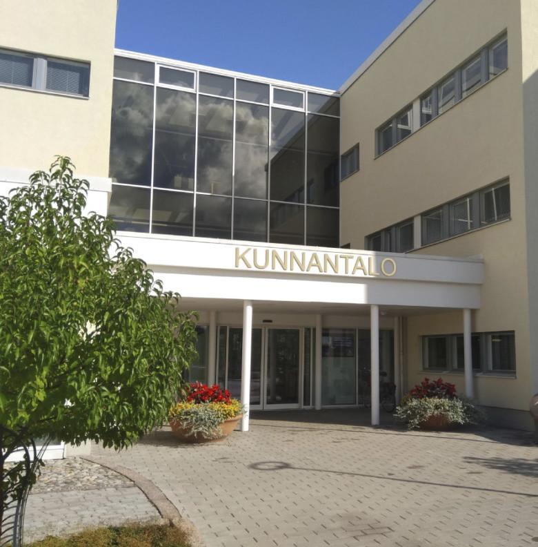 Kunnantalon pääsisäänkäynti kesäaikaan. Kesäkukkaistutuksia ja koristepuu.