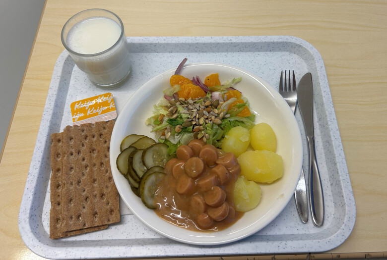 Tarjottimella koululounas, lautasella perunoita, nakkikastiketta, salaattia, maustekurkkua. TArjottimella lisäksi näkkileipää, levitettä ja lasillinen maitoa.