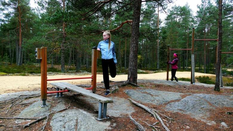 Tyttö ja nainen ulkoiluradan kuntolaitteiden luona venyttelemässä.