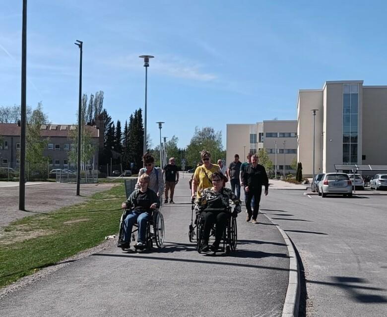 Ryhmä henkilöitä kävelee kaupungintalon viereistä jalkakäytävää pitkin. Kaksi heistä liikkuu pyörätuolilla.