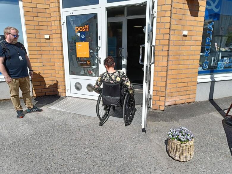 Henkilö pyörätuolin kanssa liikkeen sisäänkäynnillä.