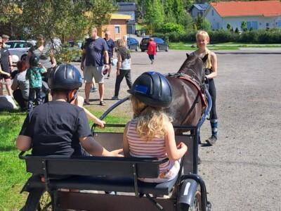 Lapset istuvat hevosen vetämissä kärryissä, taustalla ihmisiä.