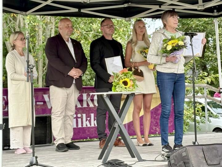Henkilö pitää kiitospuhetta, taustalla neljä muuta kuuntelemassa.