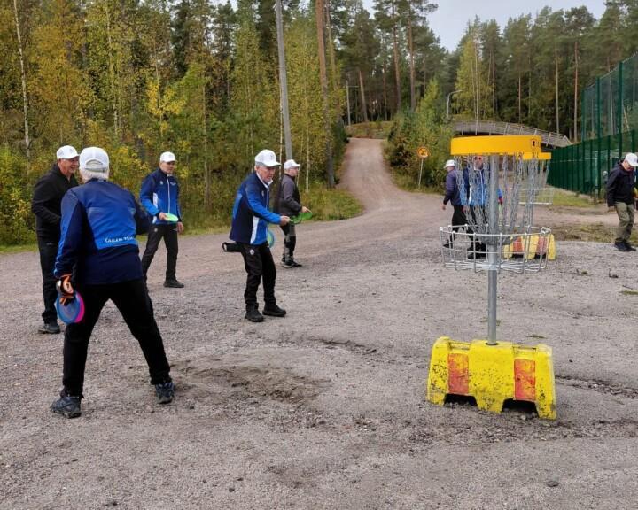 Miehiä heittämässä frisbeegolf-kiekkoja koriin.